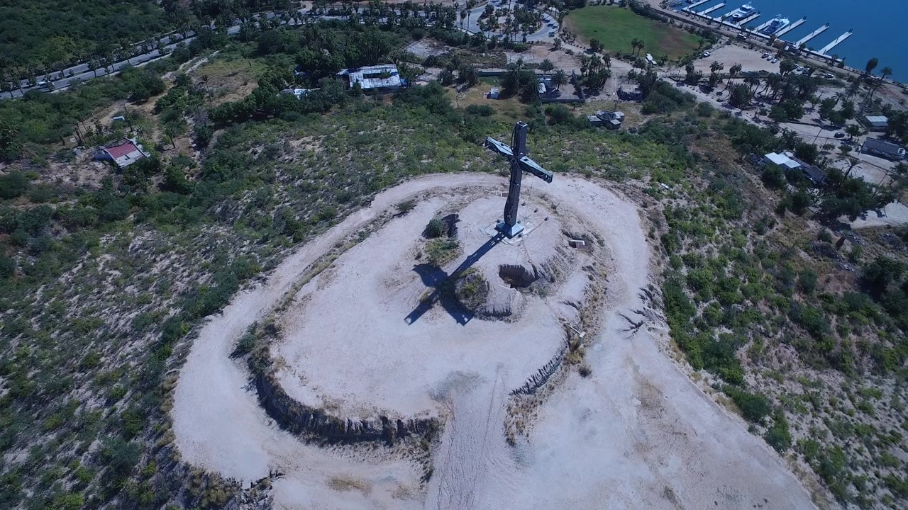 Aerial angle on a large cross casting a shadow across a dry hilltop.
