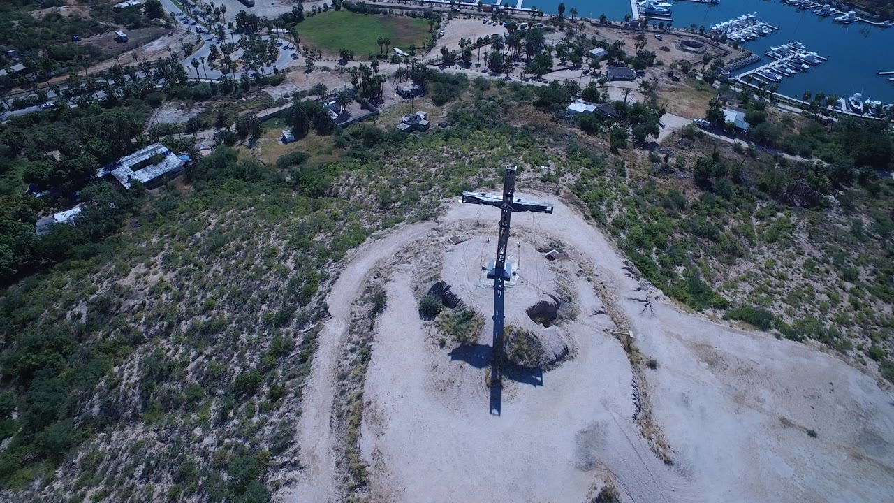 Aerial view of a cross on a scrubby hill above a marina.