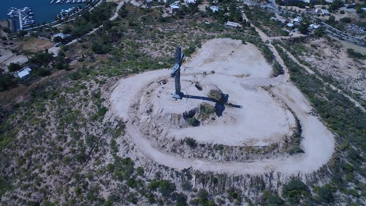 Aerial view of a tall crucifixion monument on a pale rocky hilltop.