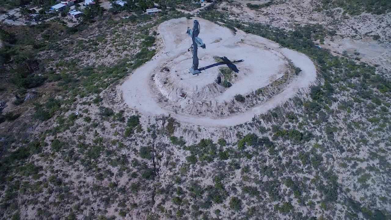 Aerial view of a large cross on a pale dirt mound in scrubland.