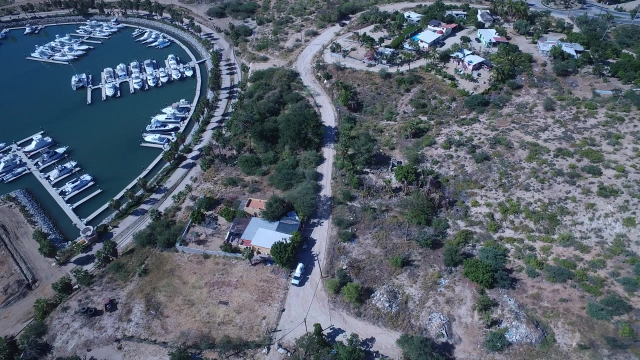 Overhead view of marina docks, moored boats, road, scrubland, and small buildings.