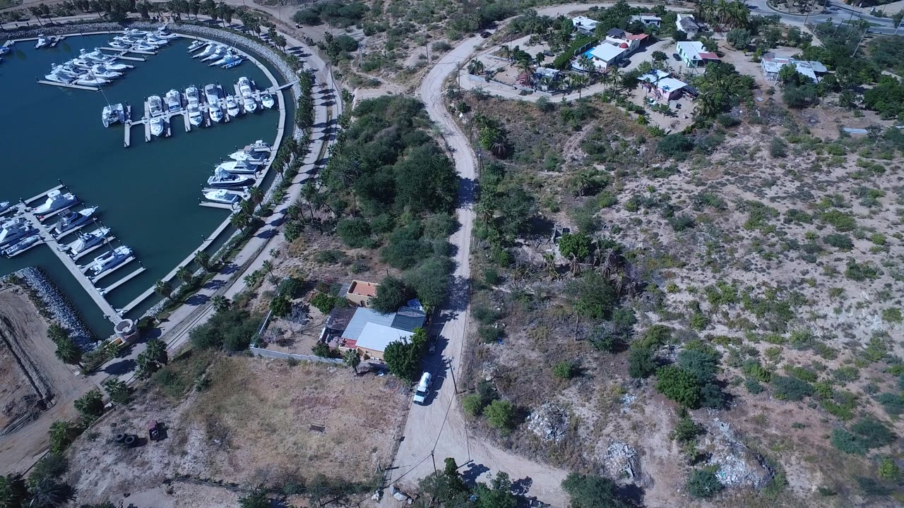 San Jose del Cabo aerial view with the marina occupying the left side, rows of boats on finger docks, dry brush lots to the right, and no visible people.