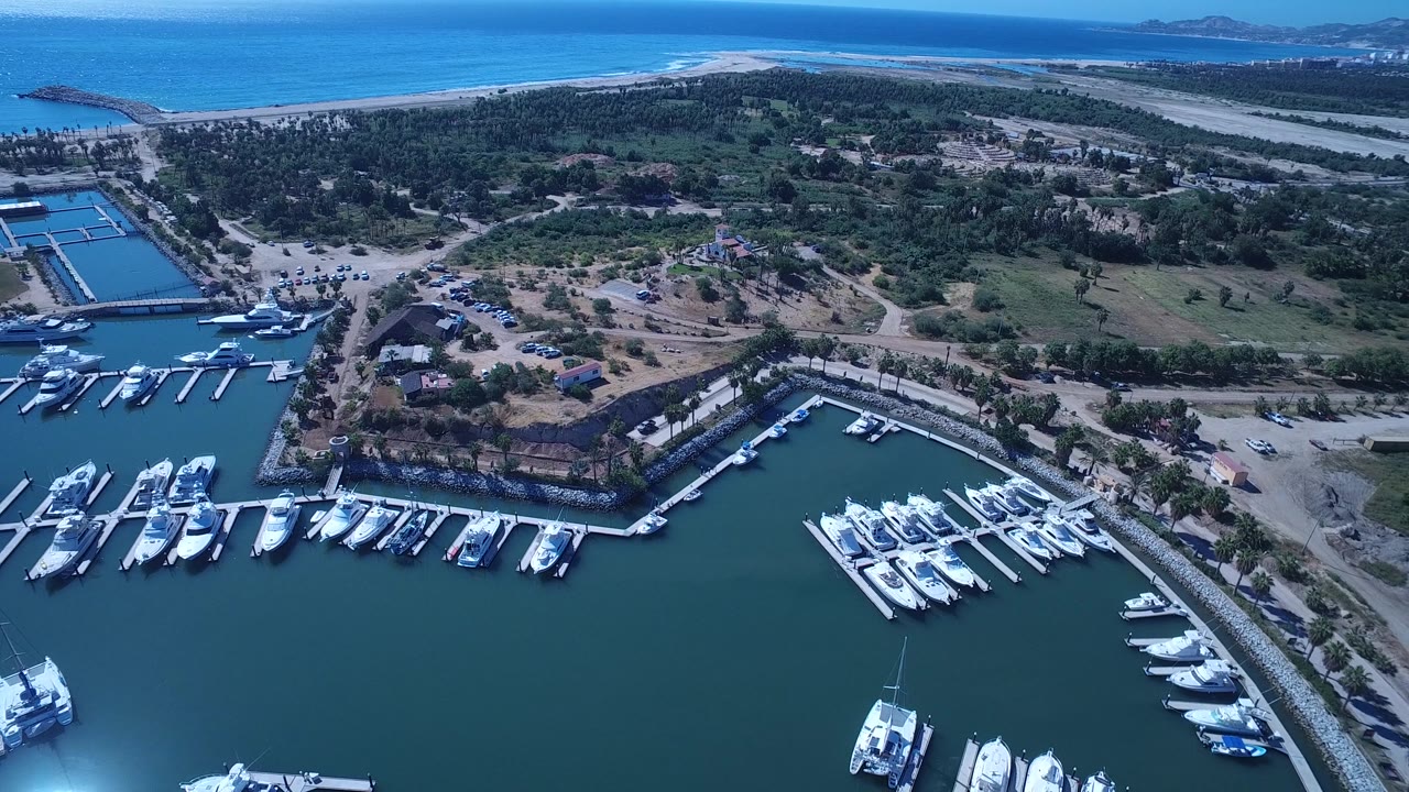 Drone view across marina slips, inland greenery, roadways, beach, and ocean.