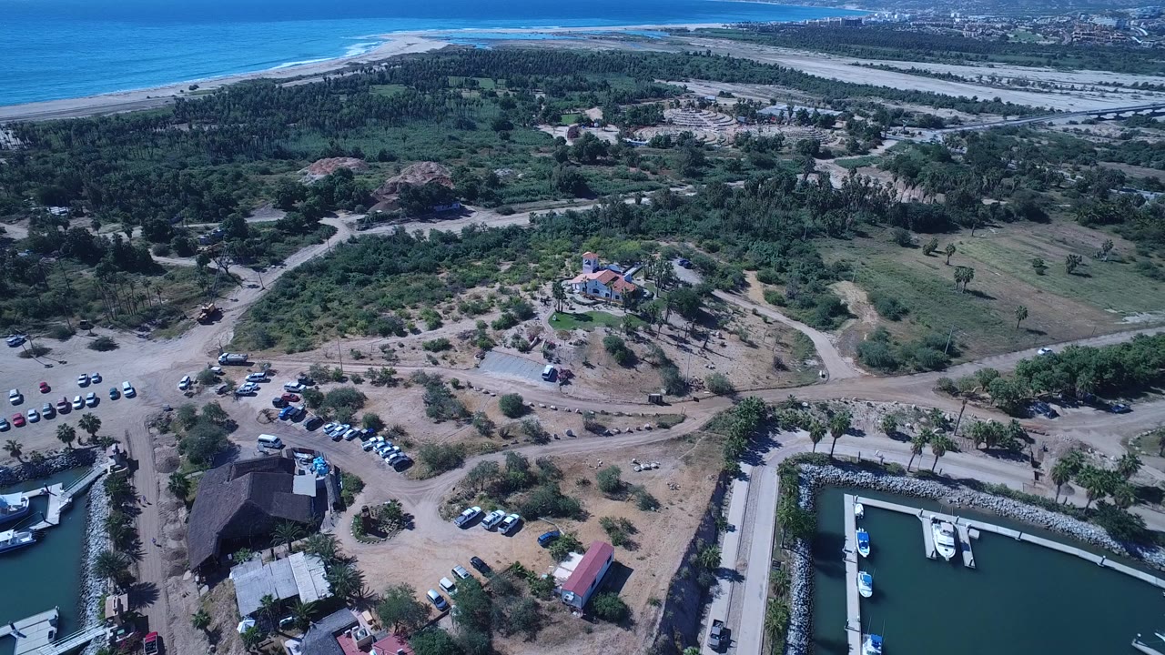 Aerial view of coastline, scrubland, roads, parked cars, and a marina basin.