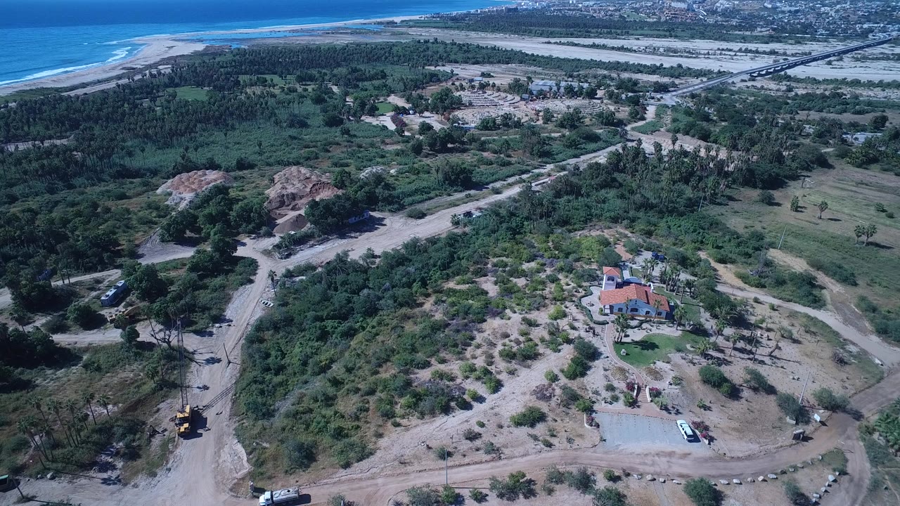 Aerial view of beach, trees, dirt roads, and red-roofed house near the coast.