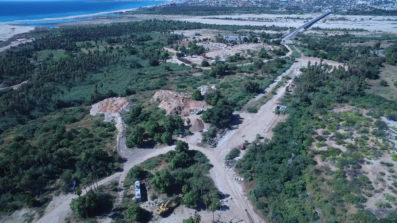 Aerial view of wooded land, dirt roads, and ocean in the distance.