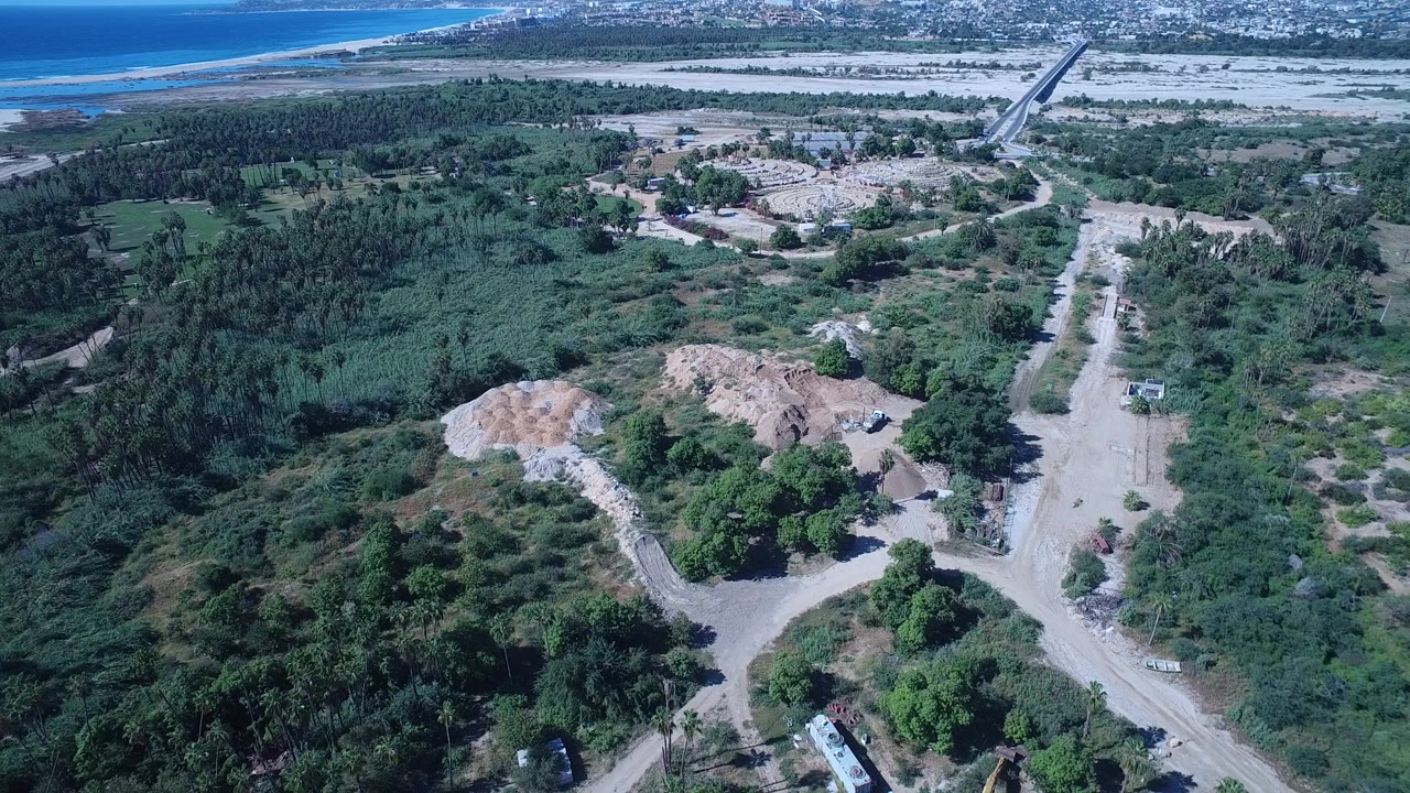 Aerial view of green terrain, dirt roads, and distant coastline.