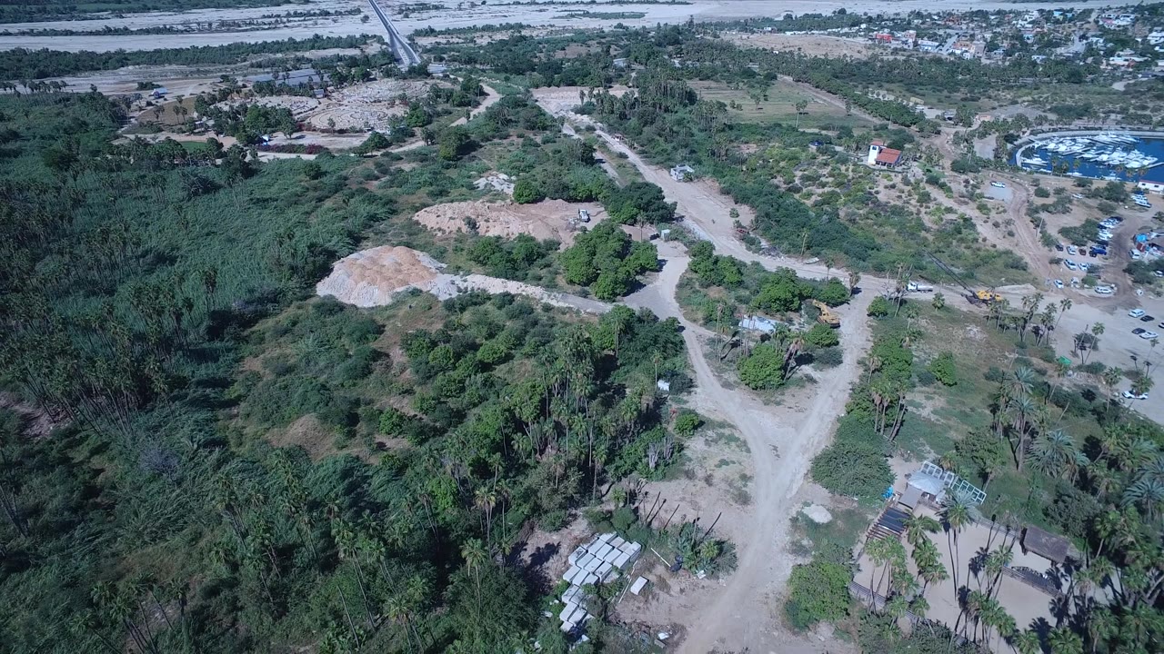 Aerial landscape with green vegetation, sandy paths, and marina boats at upper right.