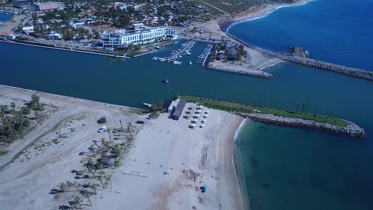 Aerial view of sandy beach, inlet water, breakwaters, and shoreline buildings.