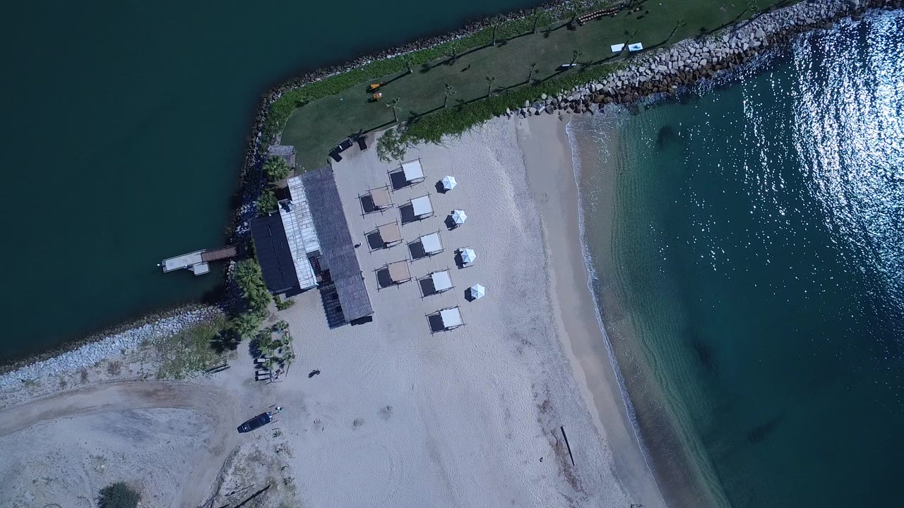 Overhead view of beach shade structures beside blue coastal water.