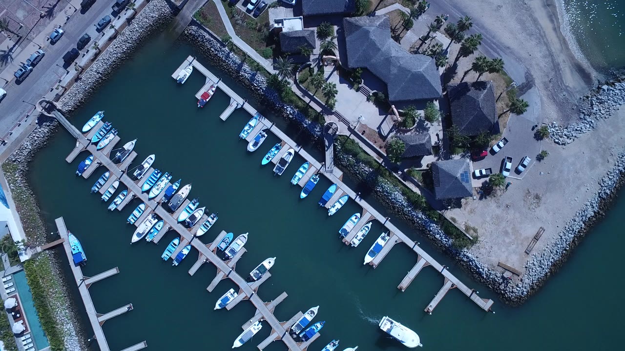 Overhead marina with boats docked beside waterfront buildings and a road.