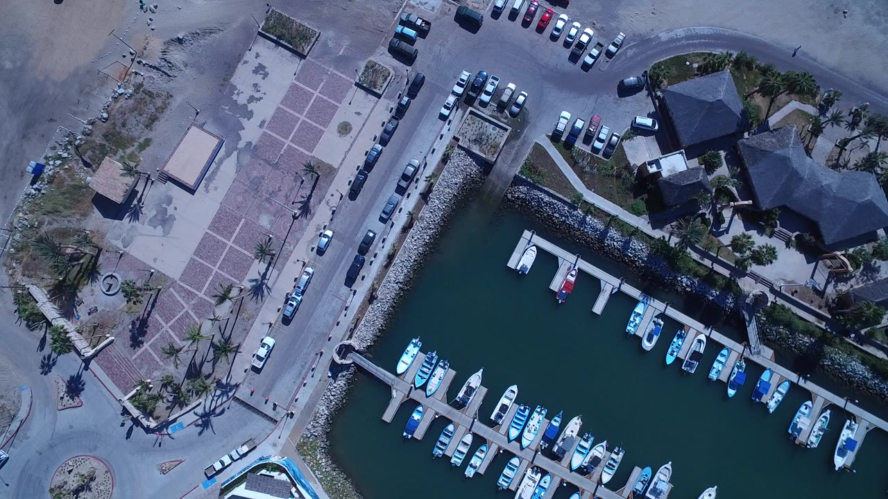 Overhead view of marina docks beside a paved plaza and parked cars.