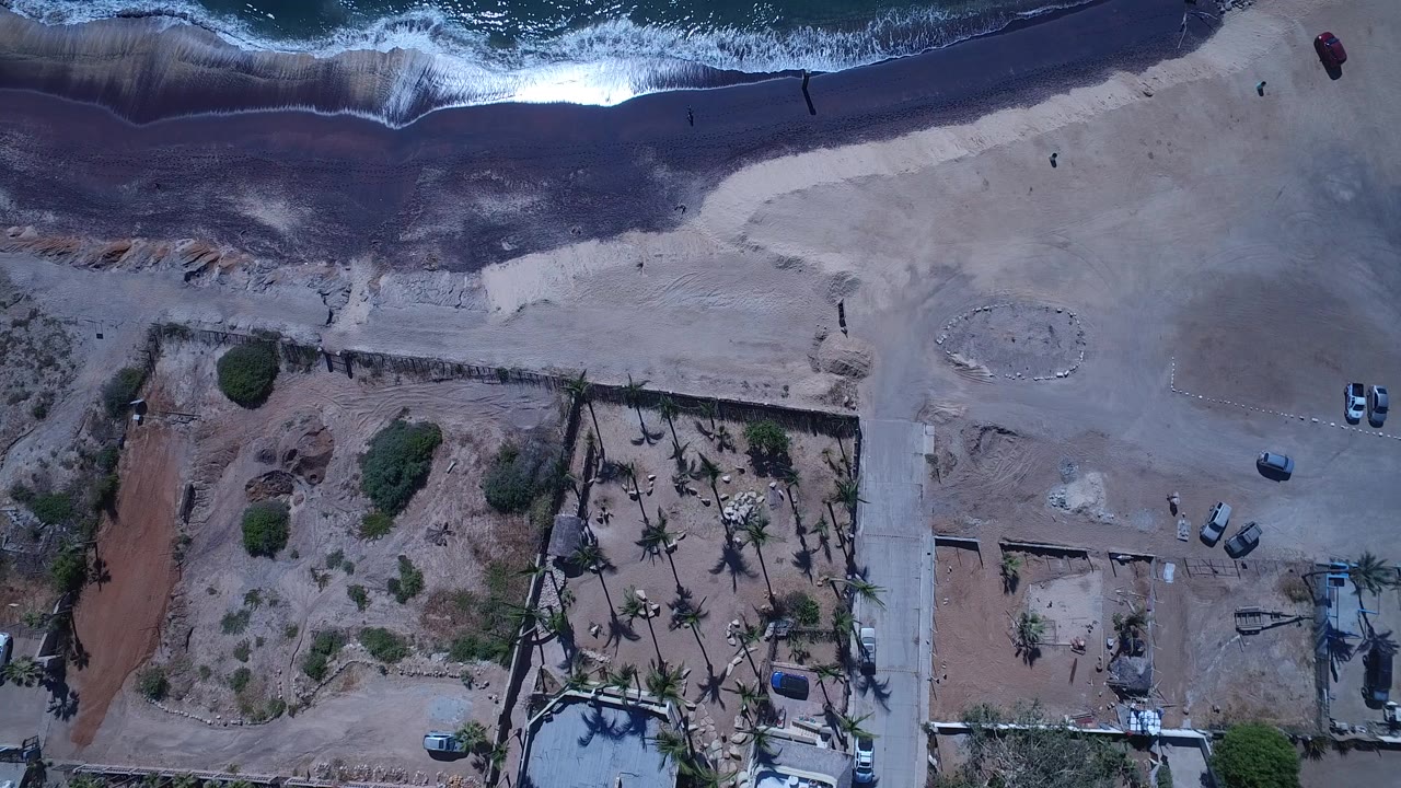 Overhead beach, surf, dirt lots, road, palms, and parked cars.