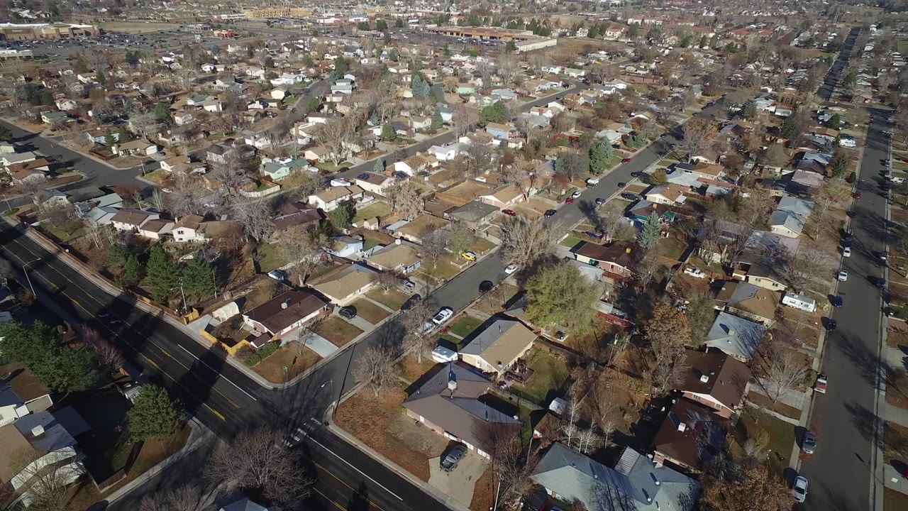 High aerial frame over Westminster, Colorado residential blocks with diagonal streets, detached houses, brown lawns, leafless trees, parked cars, and no visible people.