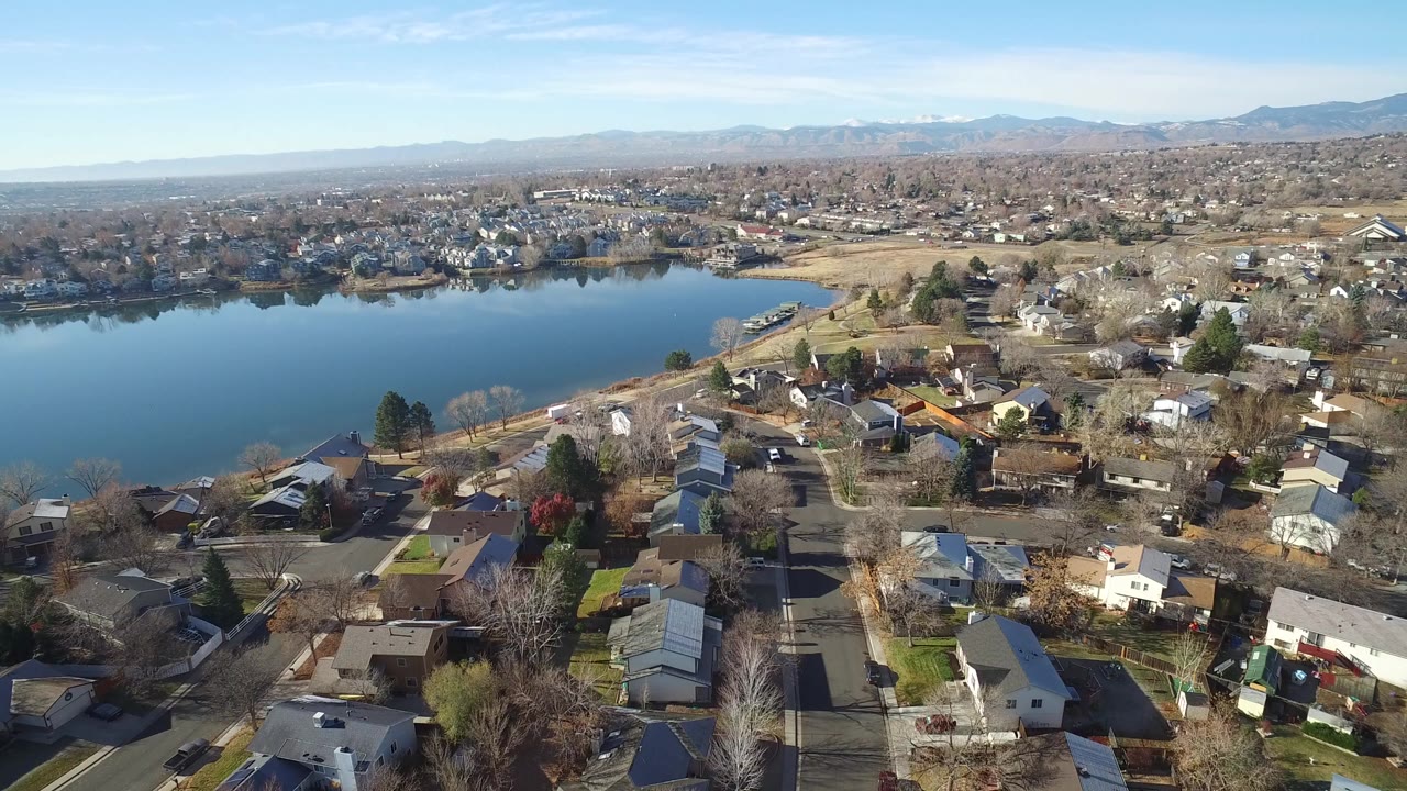Aerial view of houses, streets, pond, and distant mountains.