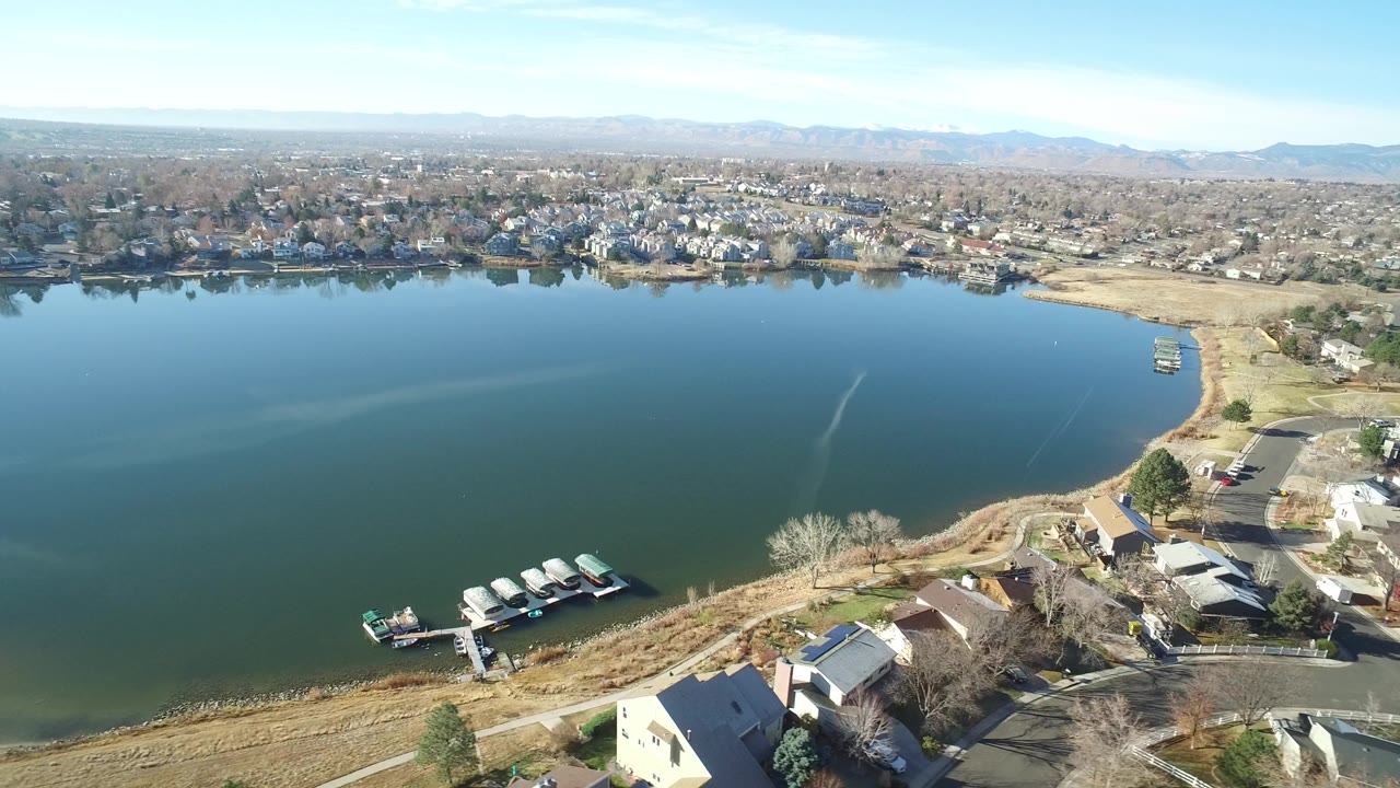 Aerial view of a lake with docks, lakeside homes, and distant suburbs.