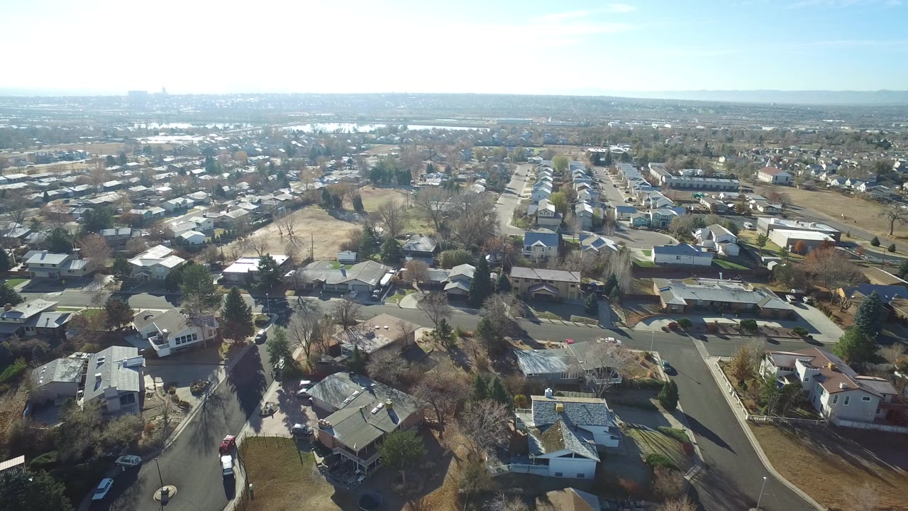 Aerial view of suburban rooftops and curved streets under bright sky.