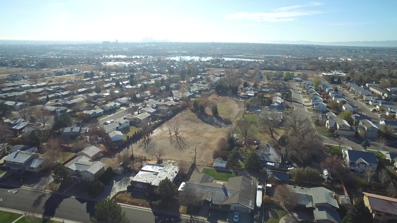 Suburban blocks and a large open field seen from above with distant skyline haze.