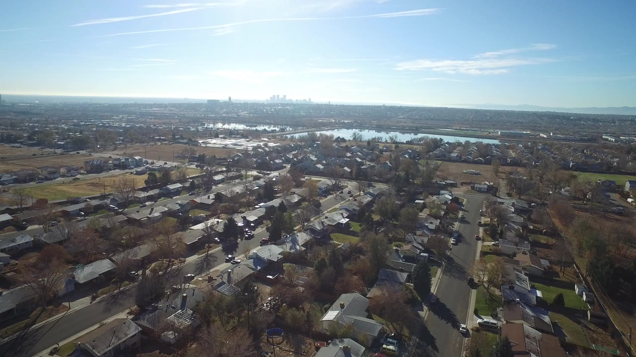 Aerial view over suburban homes toward a lake and distant skyline.
