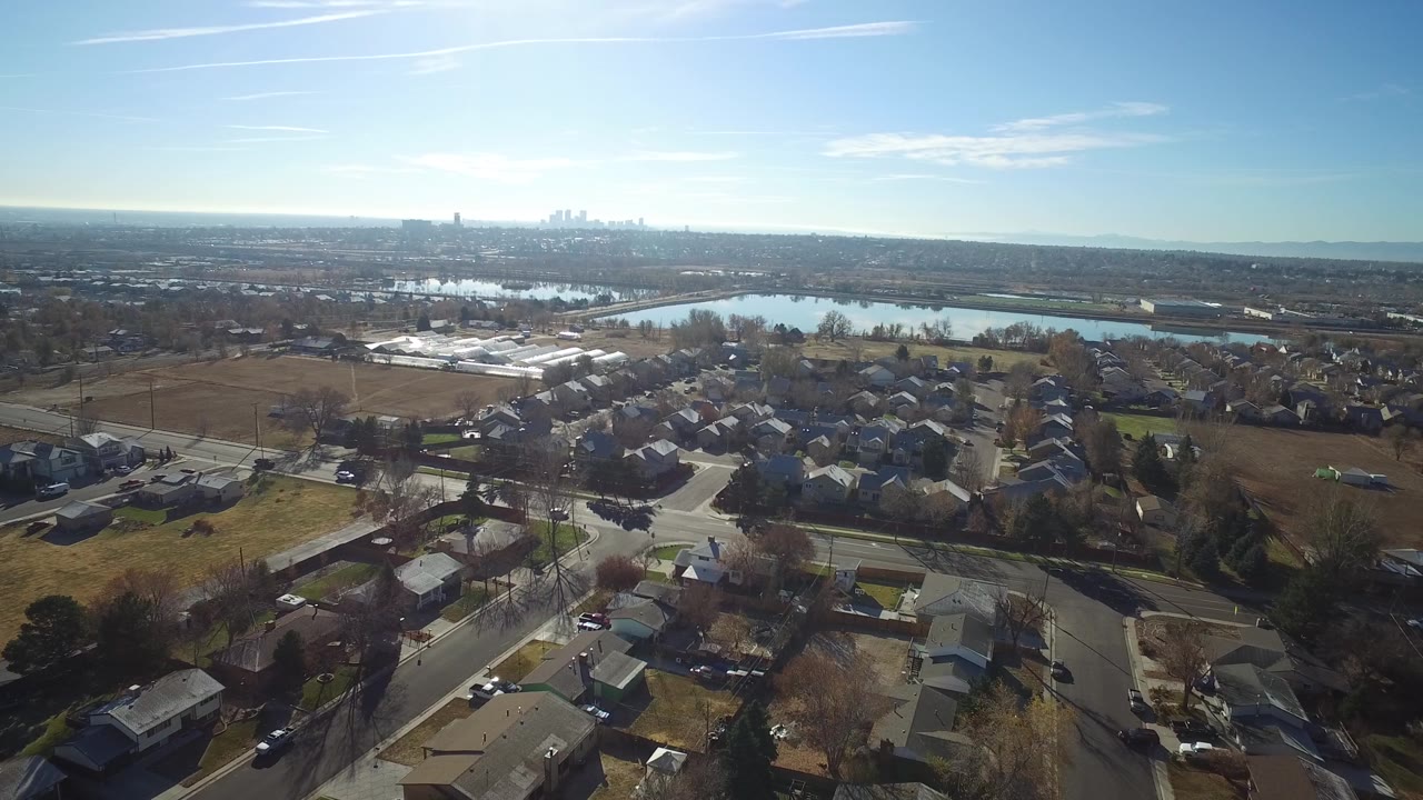 Suburban rooftops and streets seen from above with water and skyline beyond.