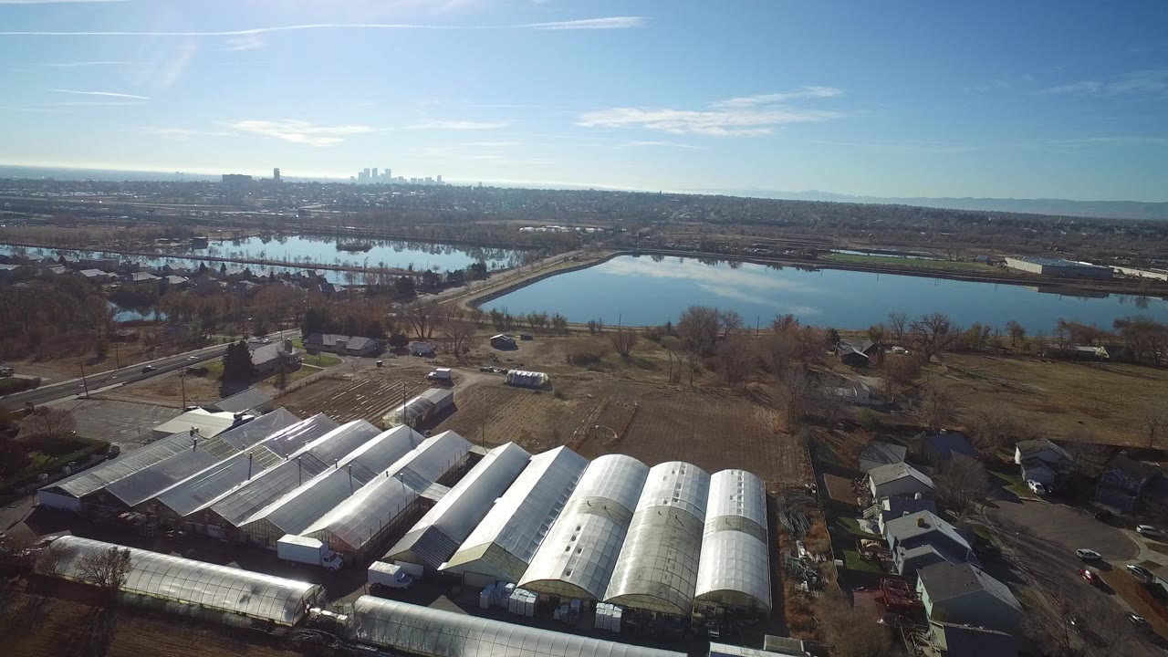 Aerial view of greenhouses, roads, lake, and distant skyline