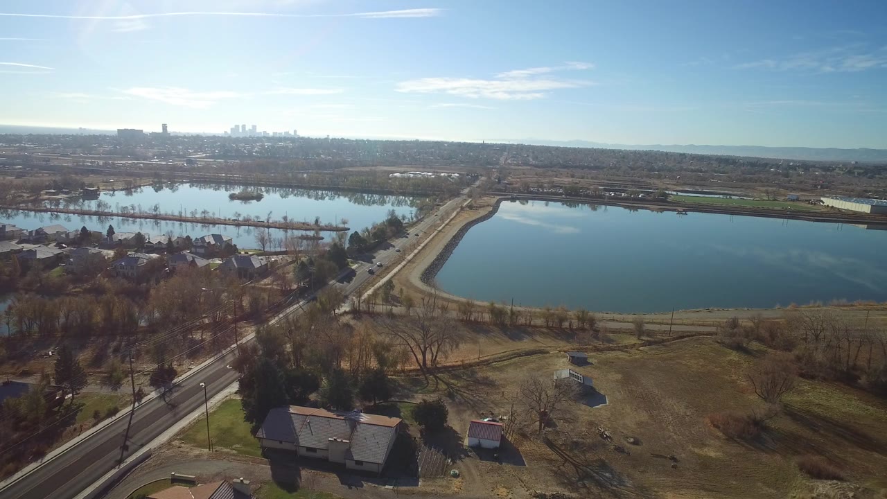 Drone view across a lake with suburban houses and roads below.