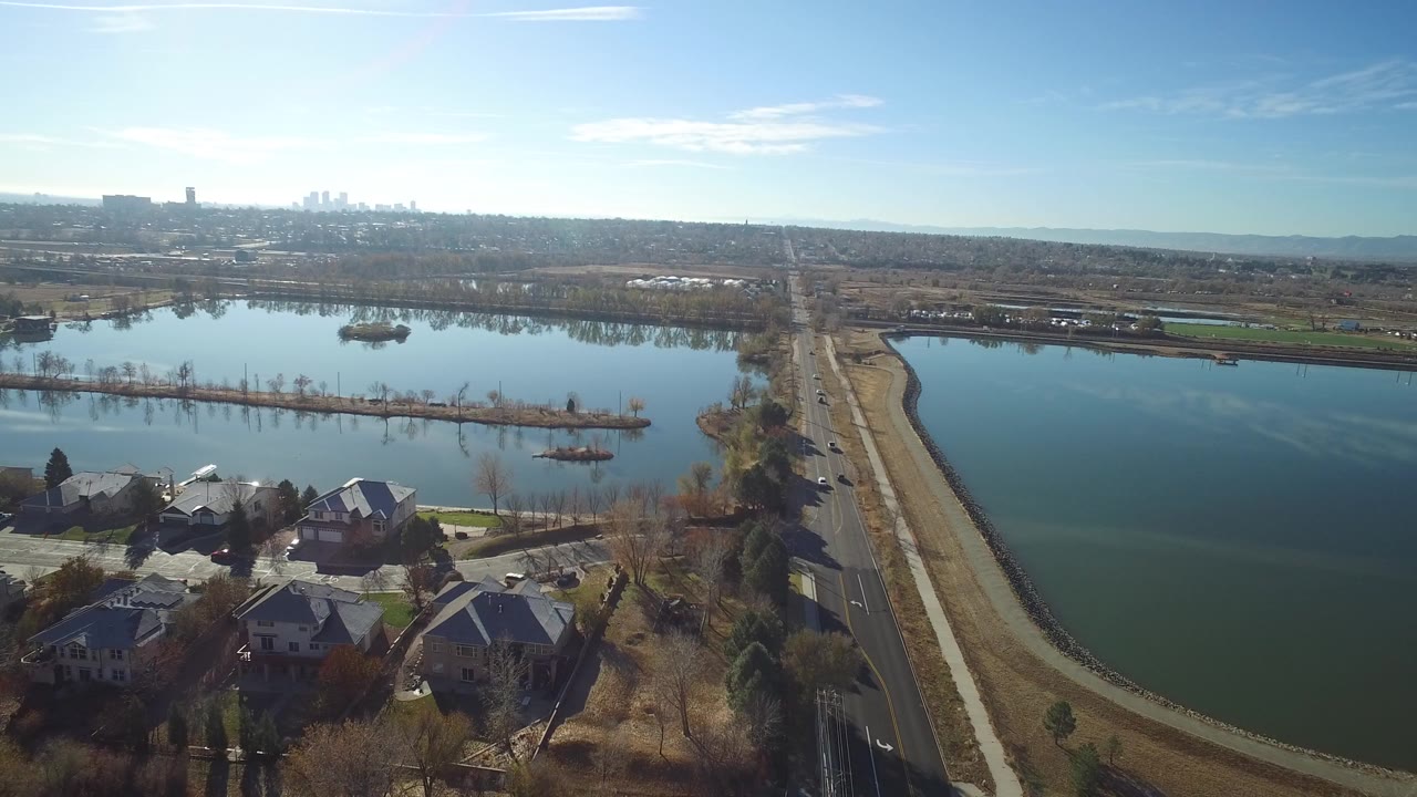 Aerial view over suburban homes, lakes, roads, and a distant skyline.
