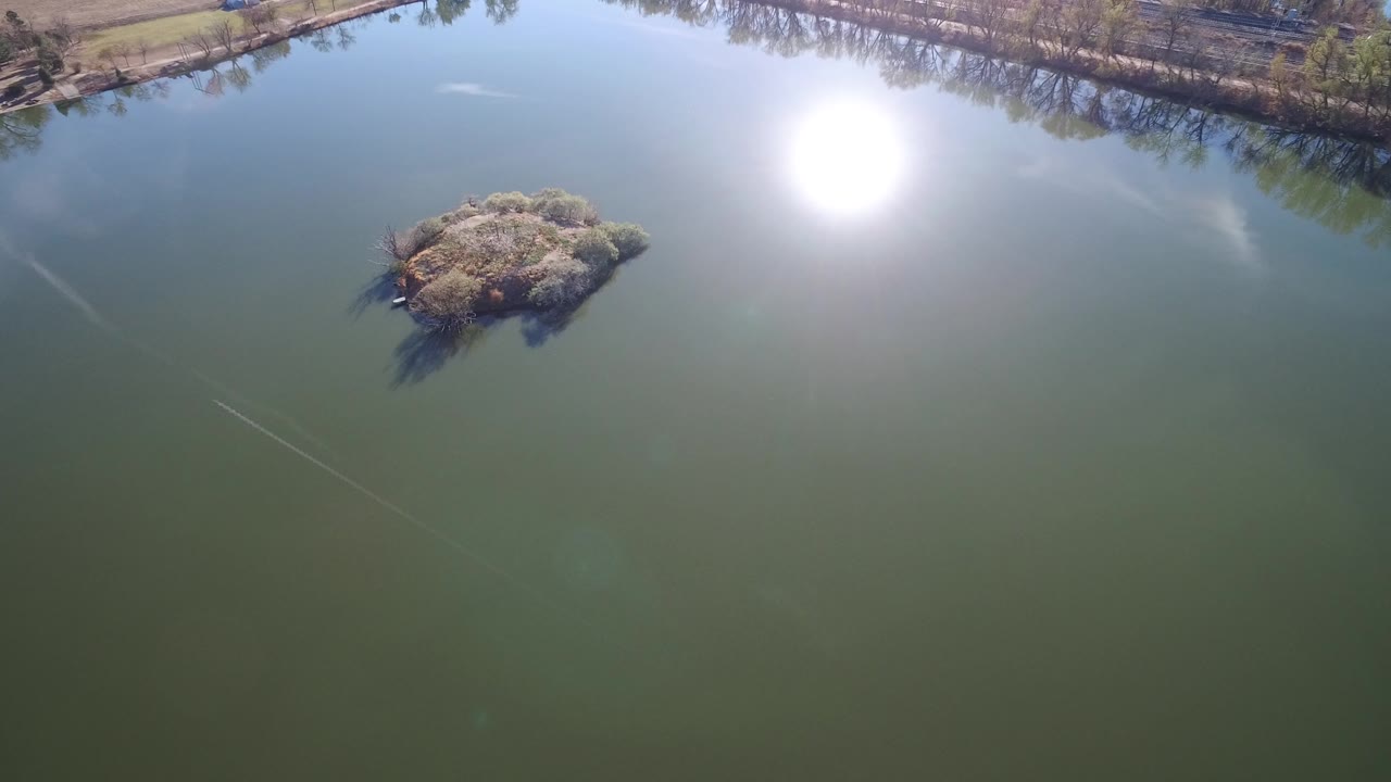 Aerial view of a small island in a lake with bright sun reflection