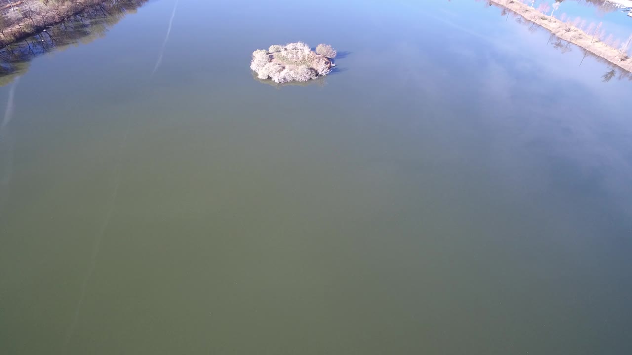 Second frame in Westminster, Colorado with the pale stone cluster slightly left of center, still water across most of the view, shoreline at the upper right, and no visible people.