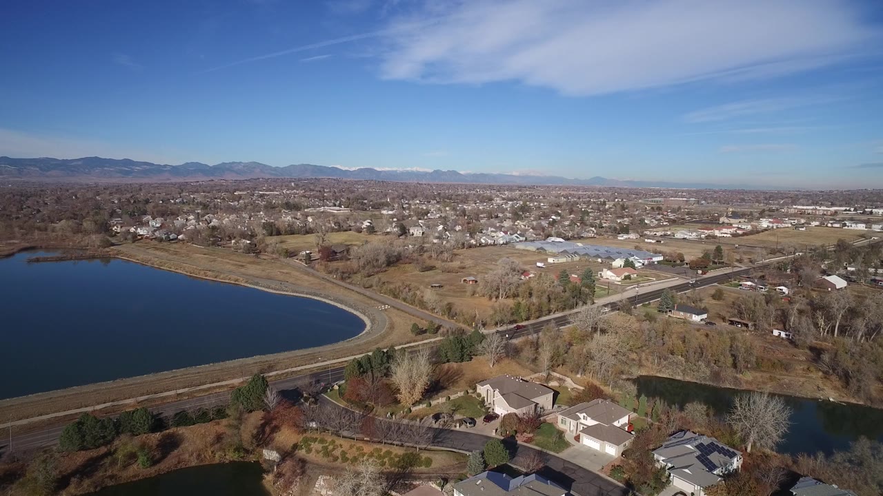 Aerial suburban landscape with lake, roads, houses, bare trees, and mountain horizon.