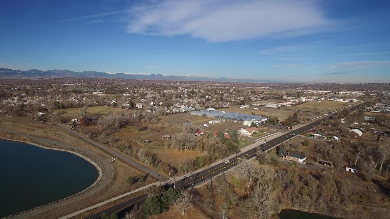 Drone view of a striped road, reservoir, houses, fields, and distant mountains.