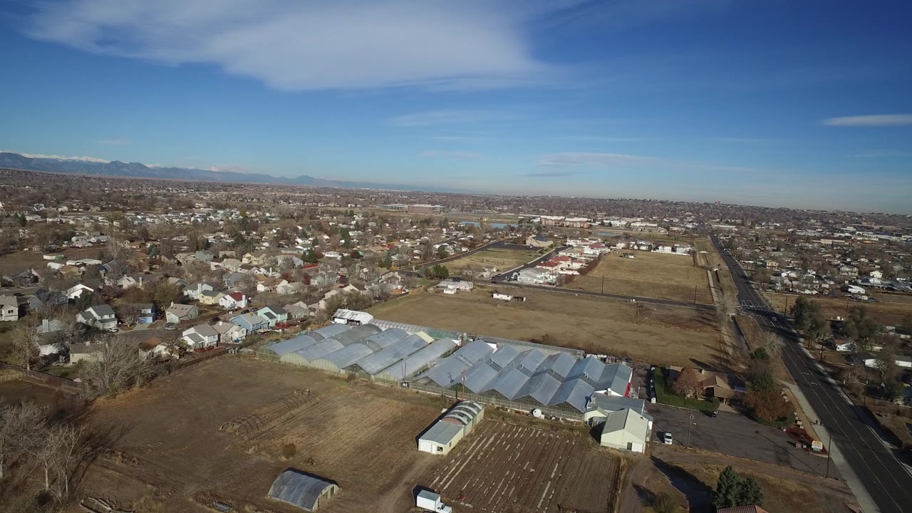 Aerial view of suburban homes, greenhouses, fields, roads, and distant mountains.