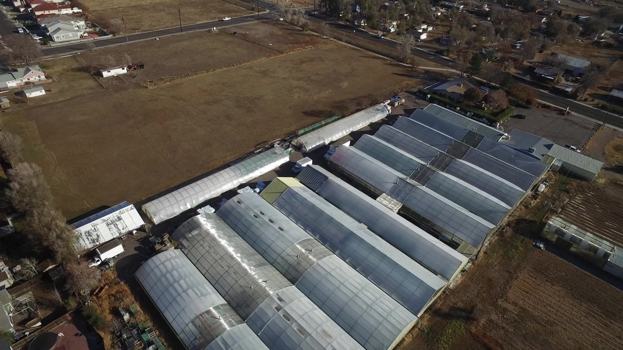 Overhead drone angle on warehouse roofs with a field and neighborhood edge behind.