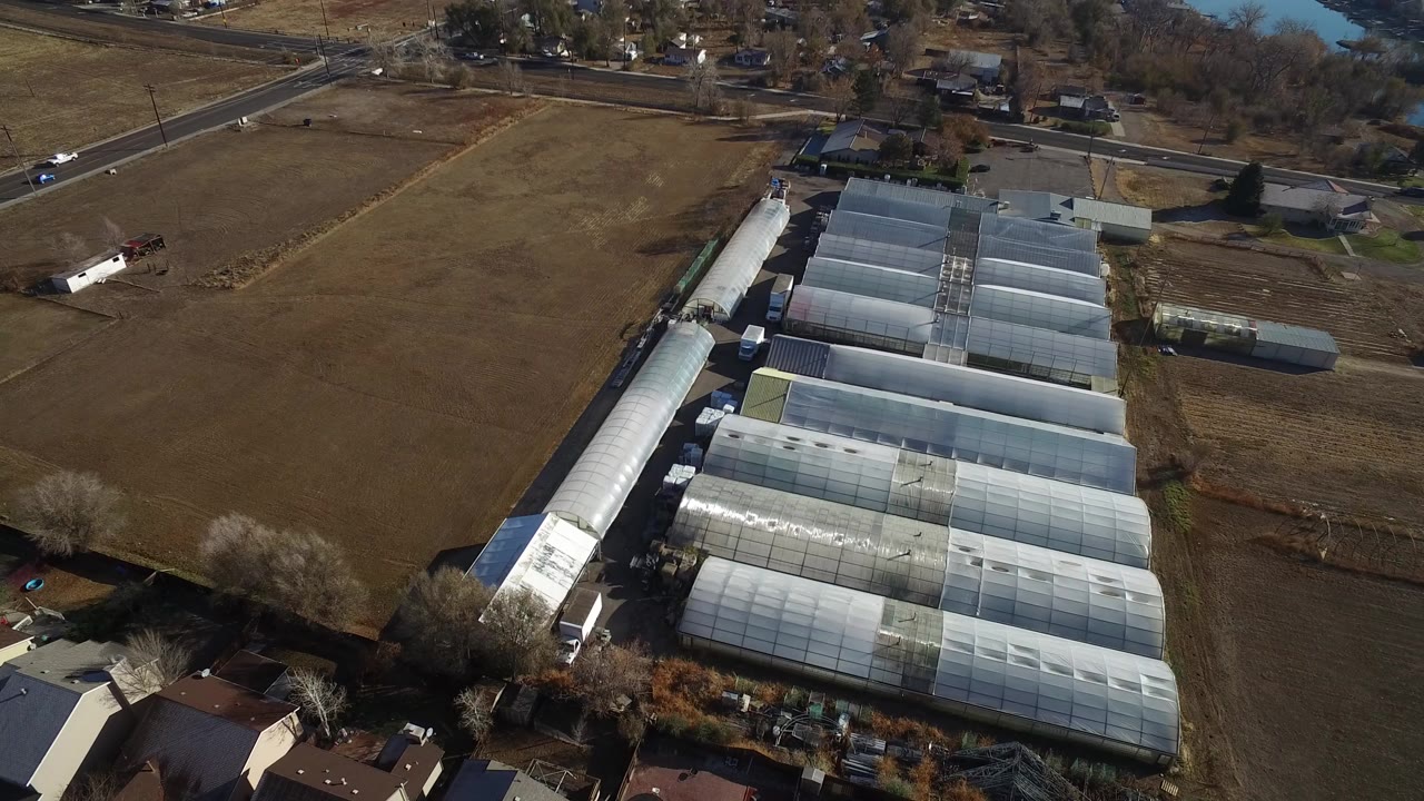 Aerial view of greenhouse structures beside brown fields and nearby homes.