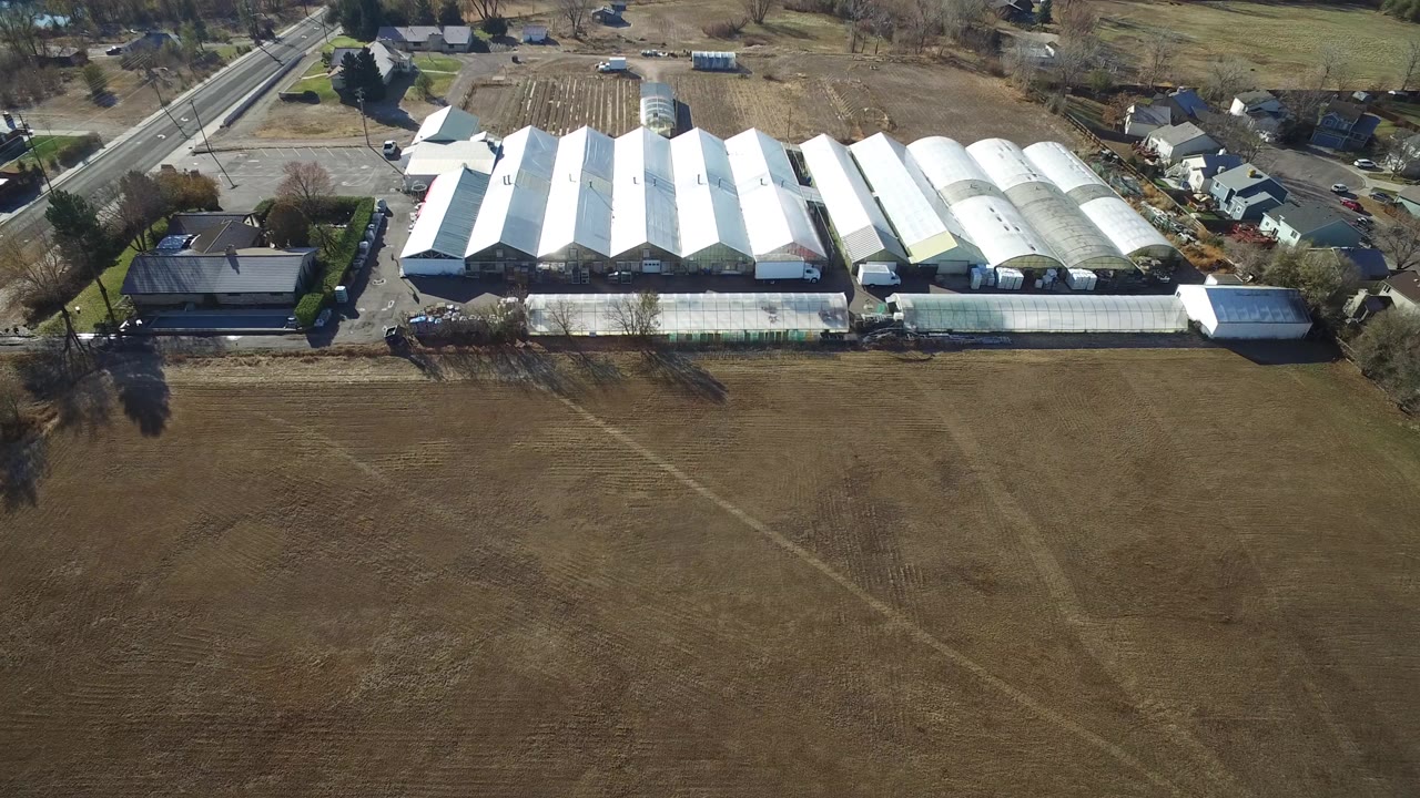 Aerial view of white-roofed industrial buildings beside brown fields and homes.