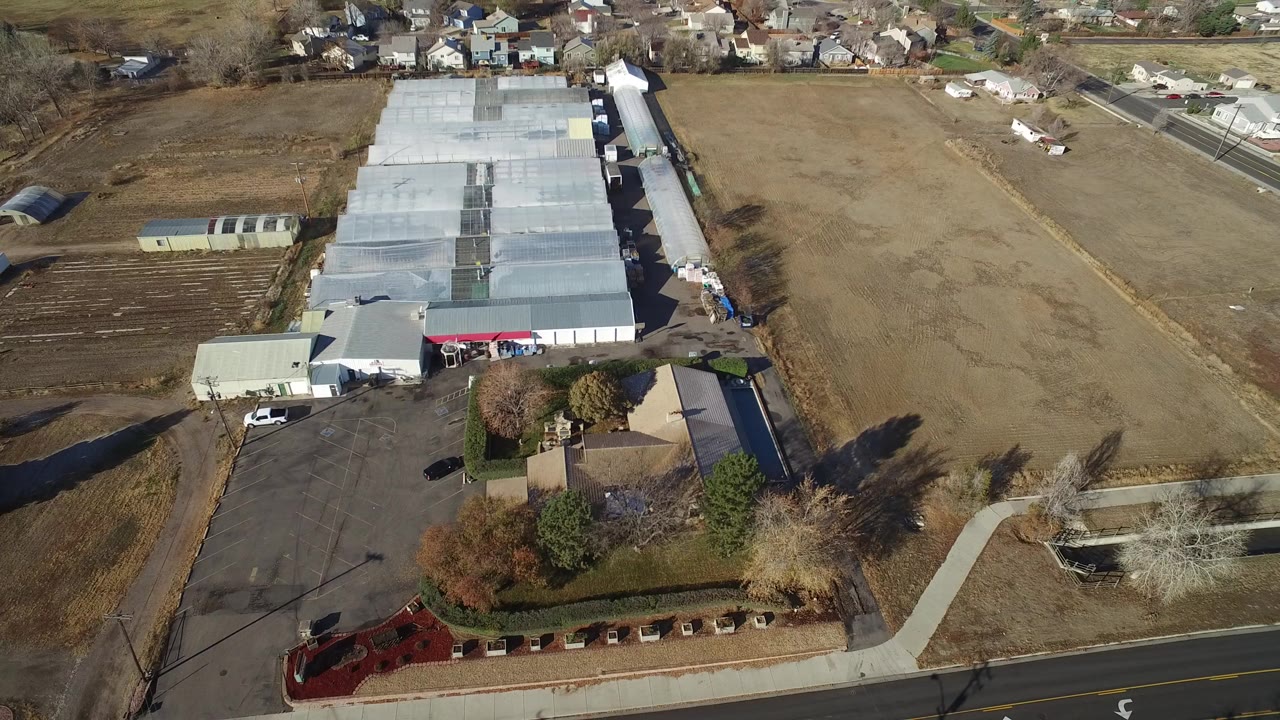 Aerial view of a large light-roofed industrial complex beside dry fields and a road.