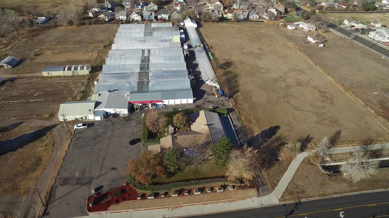 Aerial frame in Westminster, Colorado, with the industrial roofline centered, brown fields on both sides, houses along the top edge, and no visible people.