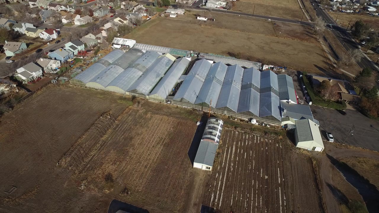 Aerial view of greenhouses, brown fields, roads, and nearby houses.