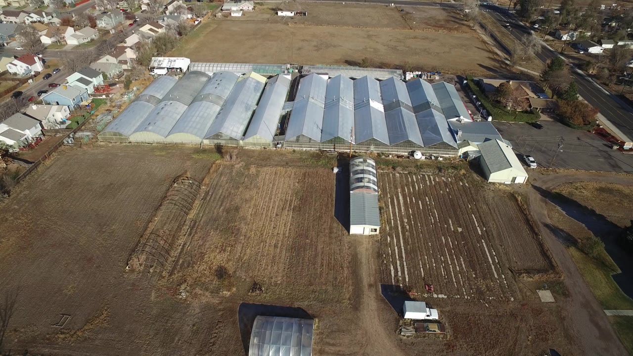 Aerial view of greenhouses, brown fields, roads, and nearby houses.