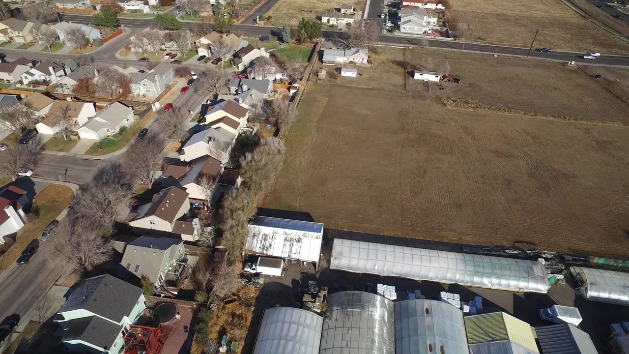 Aerial frame over Westminster, Colorado with houses clustered near a main road, brown fields in the background, several cars, bare trees, and no visible people.