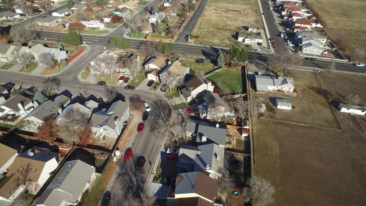 A slightly later aerial frame shows Westminster homes bordering a larger brown open lot, with cars on nearby streets and no clearly visible people.