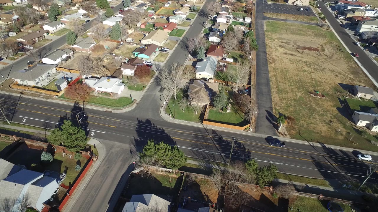 Aerial neighborhood view with a large grass lot, houses, and a road intersection.