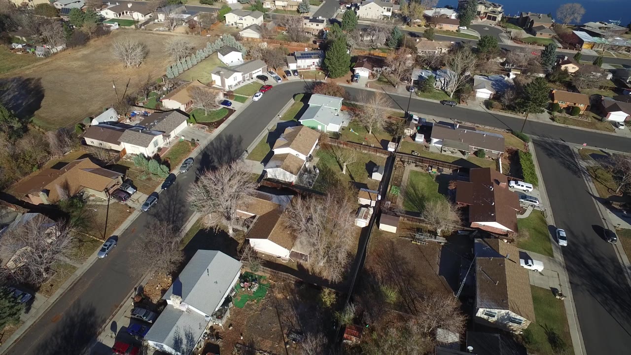 Overhead Westminster, Colorado residential view showing a curved street, light-roofed houses, fenced backyards, parked cars, winter lawns, and no visible people.