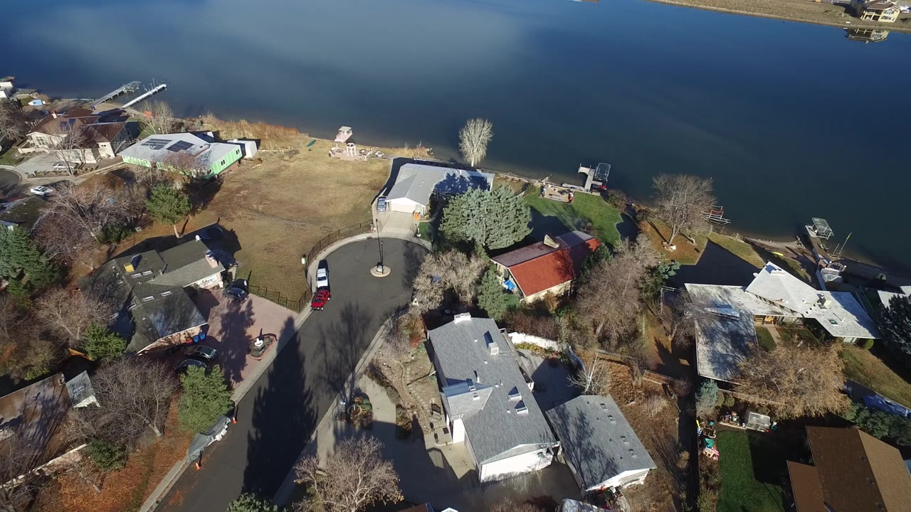 Overhead view of lakeside homes, yards, trees, and a cul-de-sac beside blue water.