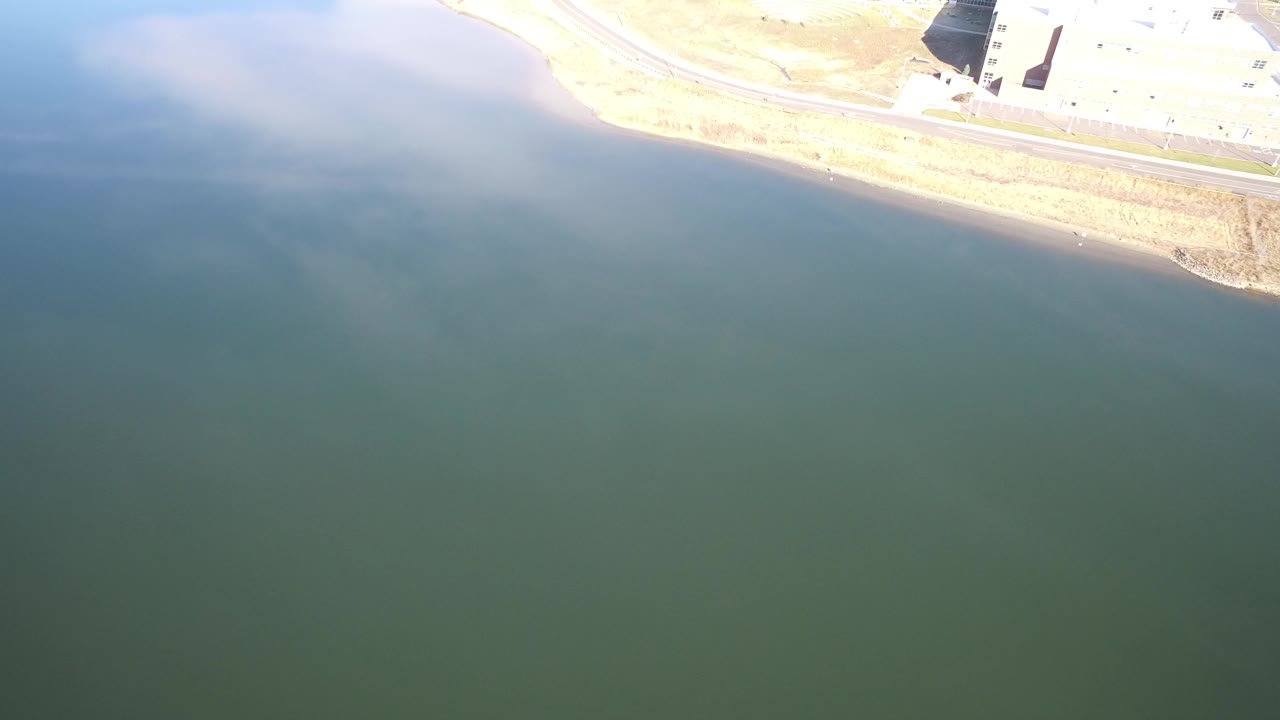 Aerial view of green-blue water beside a bright shoreline and road.