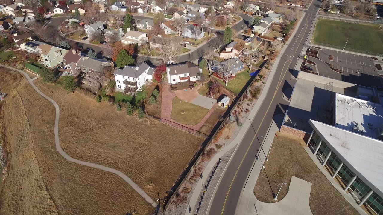 Aerial view of a road beside an open field and suburban homes.