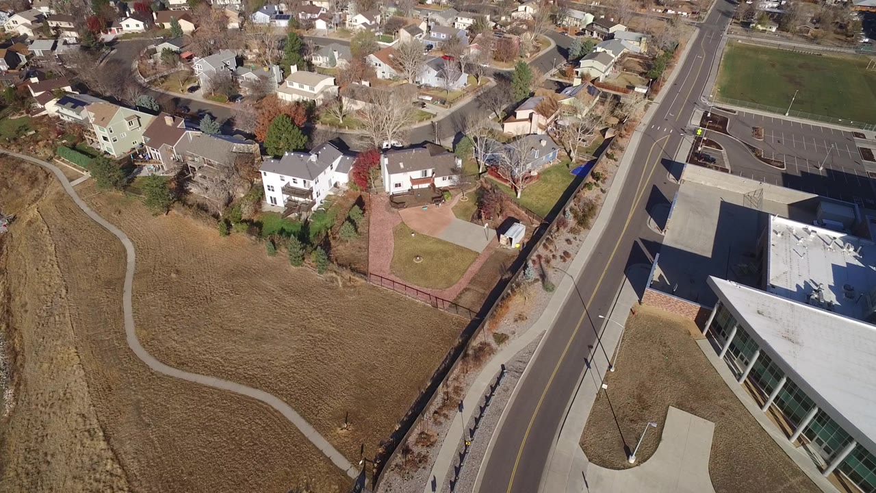 Elevated Westminster, Colorado view with houses across the top, a straight road through the frame, a brown field at left, a large flat roof at right, and no visible people.