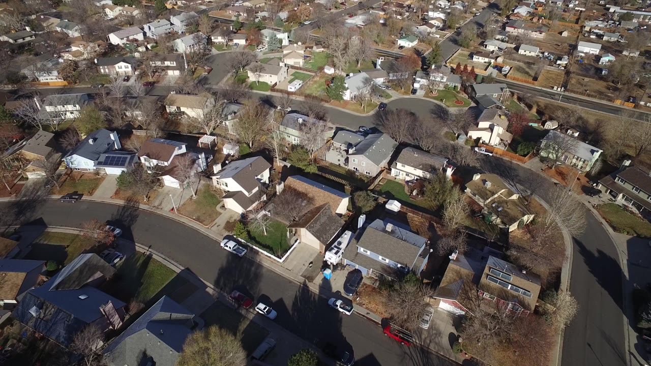 Aerial frame over Westminster, Colorado showing small detached houses, curved neighborhood roads, parked vehicles, bare trees, and no visible people.