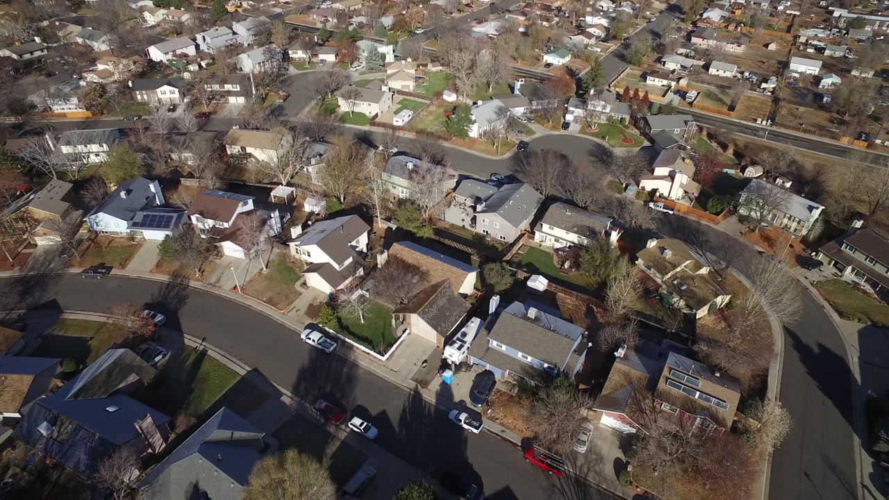 High-angle Westminster, Colorado view with rooftops, fenced backyards, a curving street, parked cars, and no visible people in the scene.