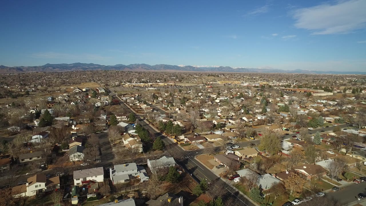 Suburban neighborhood seen from above with houses, roads, and a blue sky.